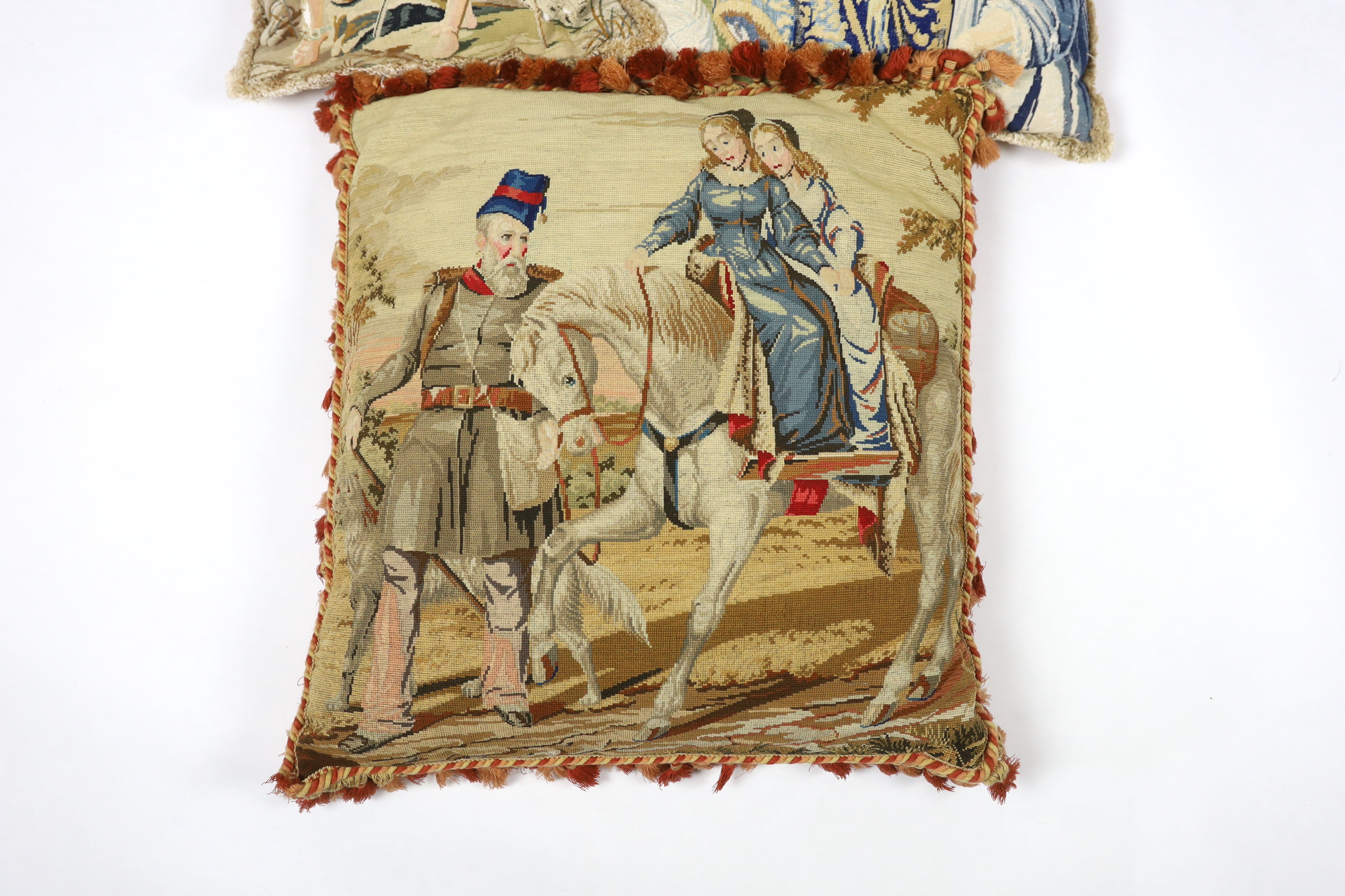 A very large Victorian Berlin wool worked cushion of possibly Queen Victoria's daughters on horseback being led by a gentleman in uniform, the cushion is edged with red tasselling, together with two similar Victorian Ber